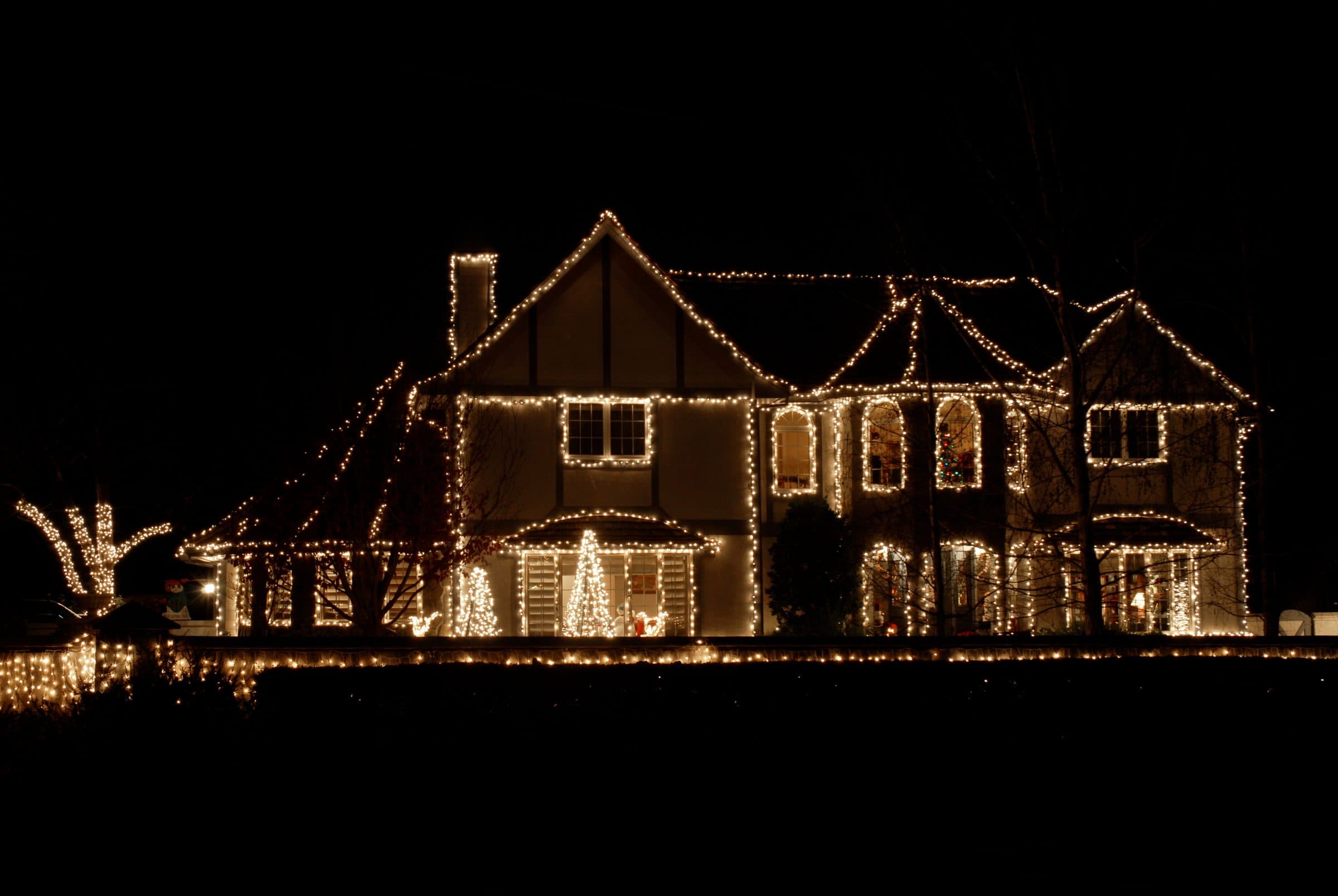 A large Tudor-style house at night with warm white lights tracing every roofline, gable and window